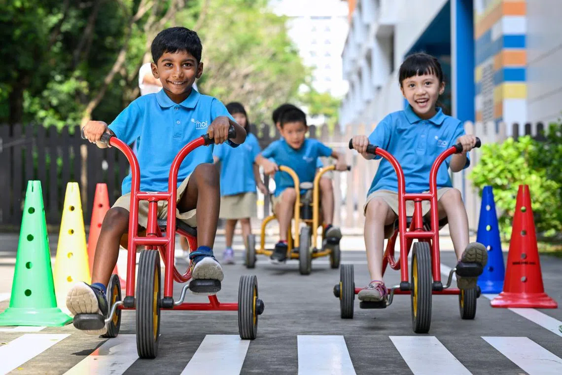 Children at MOE Kindergarten @ Punggol View riding tricycles along a mock pedestrian crossing. 