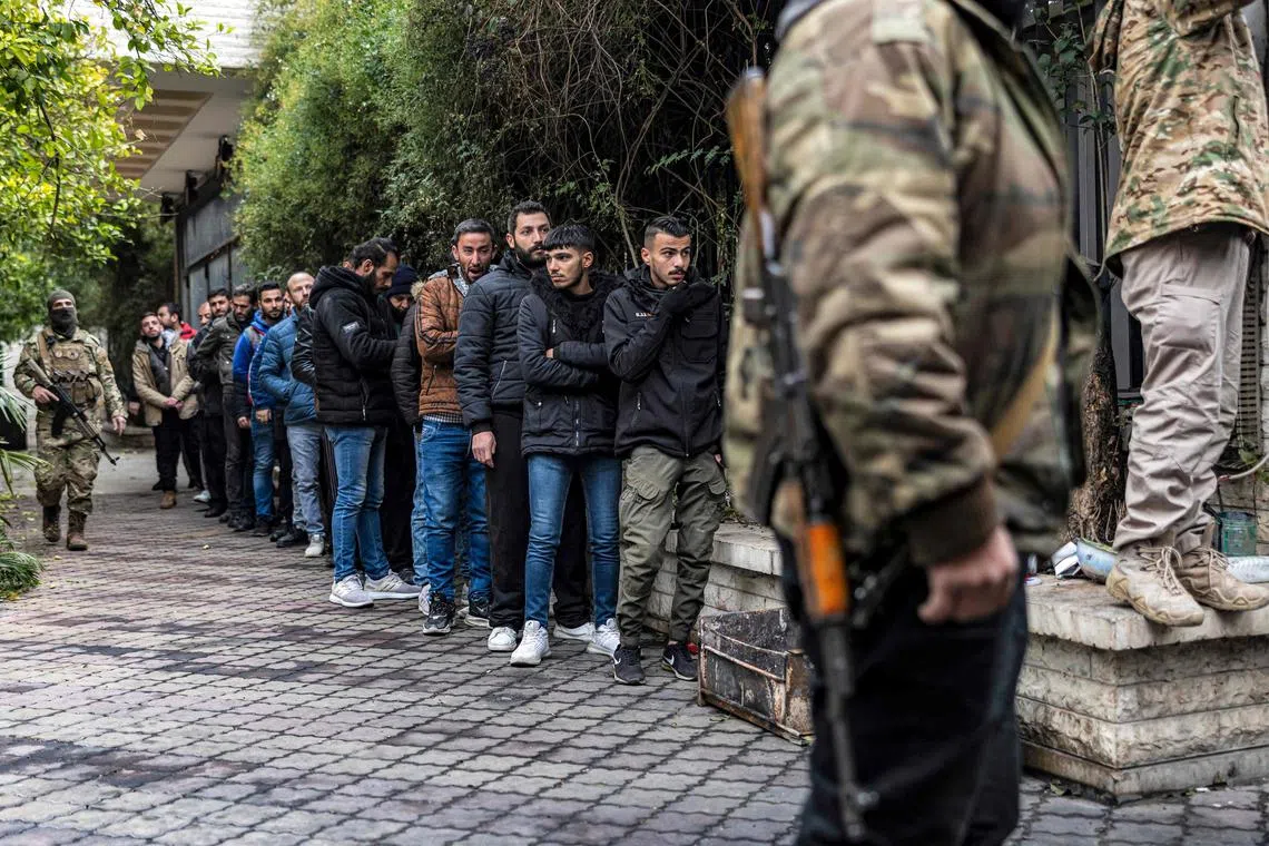 A member of Syria's security forces stands guard as former soldiers, police officers and civilians queue up at a centre for handing over small arms and security registration with the new authorities, in Damascus, on Dec 24.