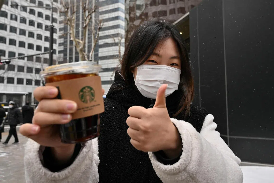 This picture taken on January 26, 2023 shows office worker Jeong Jae-won posing with an iced Americano during an interview with AFP on a street in Seoul. - K-pop stars BTS drink it. It appears in K-dramas. Fans are so dedicated to consuming it year-round they've coined a new South Korean proverb: "even if I freeze to death, iced Americano!" (Photo by Jung Yeon-je / AFP)