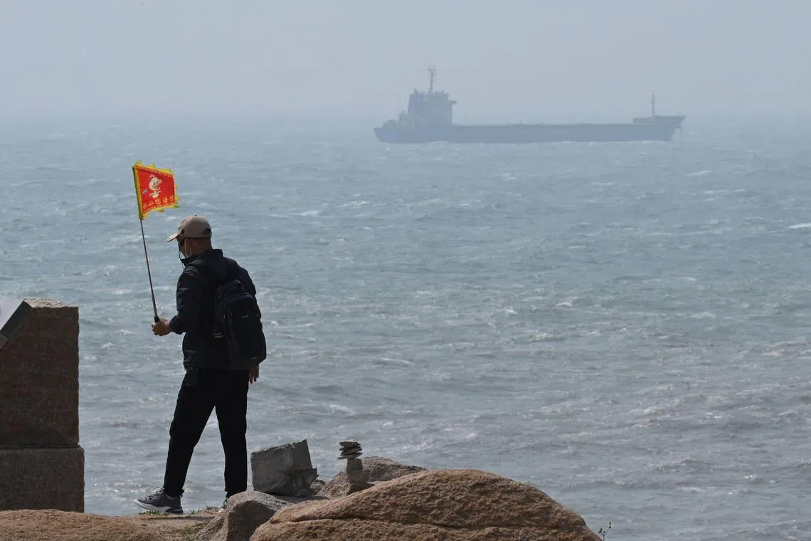 A man walks with a flag as a ship passes by behind him on Pingtan island, the closest point to Taiwan, in China’s south-east Fujian province.