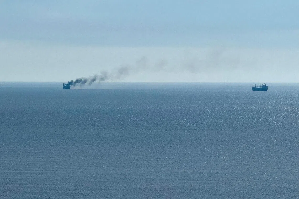 Two ships on the ocean, one emitting dark smoke.