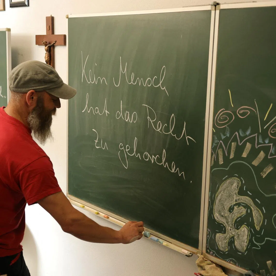 Max Heckel, a craft teacher at a secondary school who has been targeted by the local far-right Alternative for Germany (AfD) party over comments he made in class, writes on a board at his 'ANKER' event location in Arneburg, Germany, July 8, 2026. The words on the board reads \"No human being has the right to obey.\" REUTERS/Fabrizio Bensch