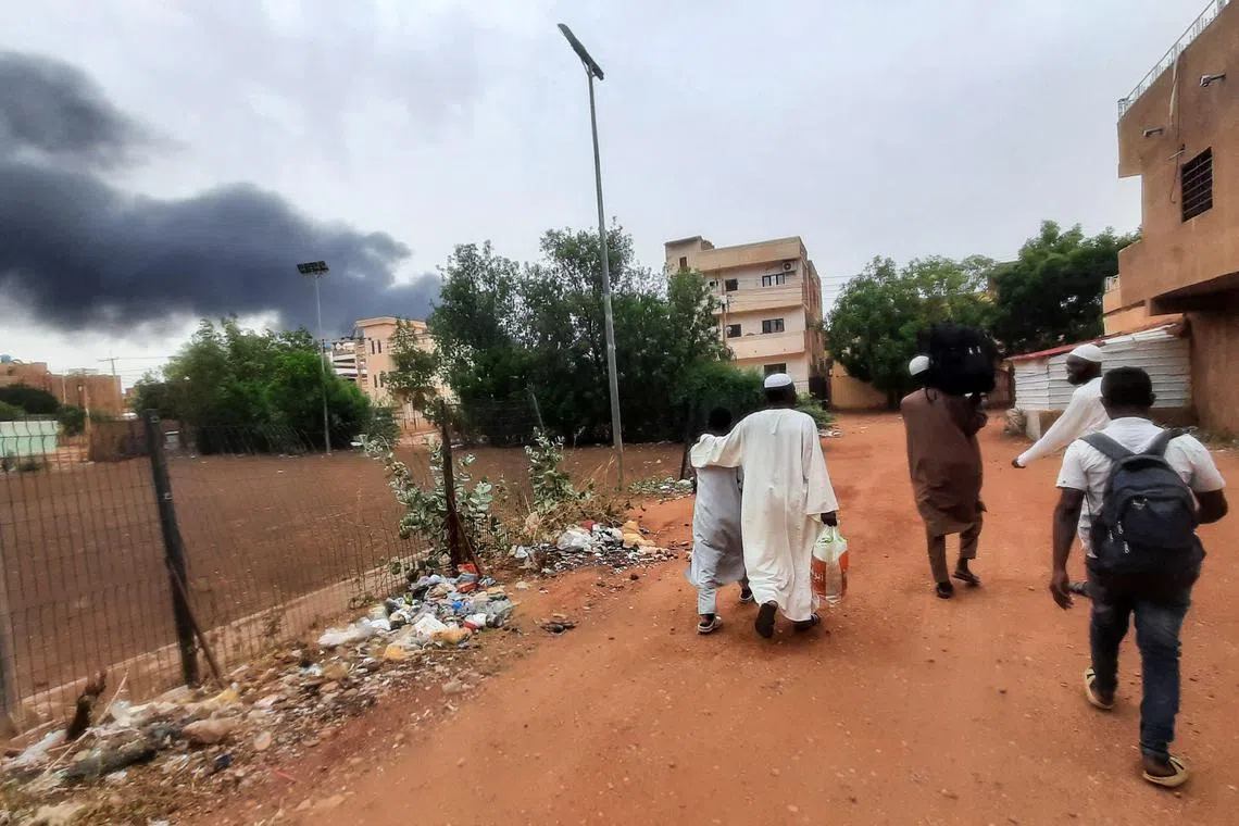 Smoke rises above buildings as people flee with some belongings, in Khartoum, Sudan, on June 10, 2023.