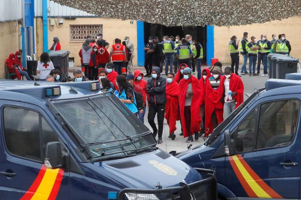 FILE PHOTO: Migrants walk outside a facility prepared for them, accompanied by members of a NGO and Spanish police officers, near the Spanish-Moroccan border, after thousands of migrants swam across this border during the last days, in Ceuta, Spain, May 21, 2021. REUTERS/Jon Nazca/File Photo