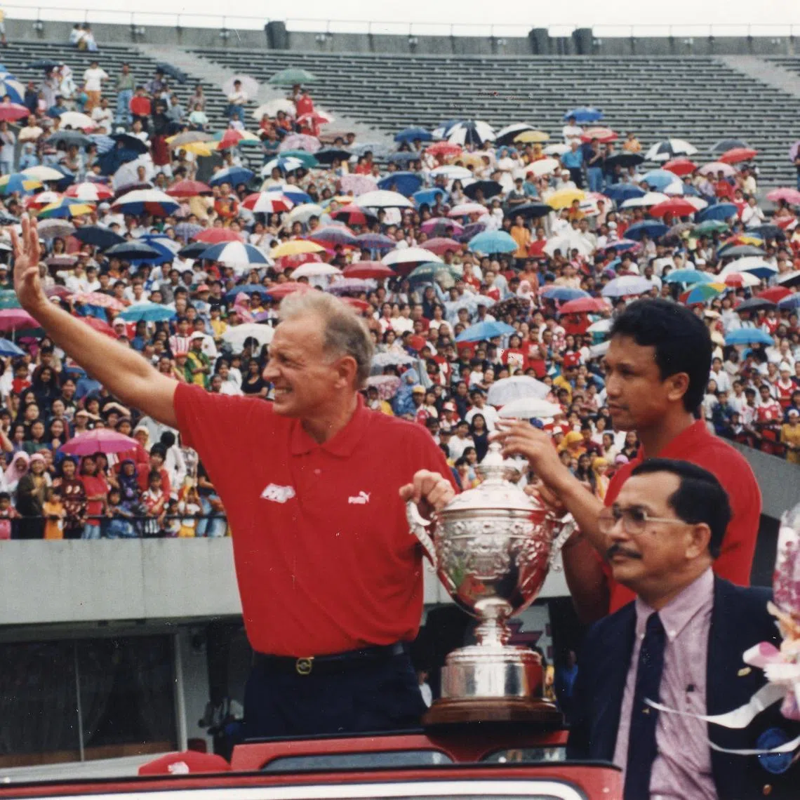 Singapore soccer coach Douglas Moore, captain Fandi Ahmad and team manager Omar Ibrahim acknowledging the cheers as they parade the Malaysia Cup before screaming fans who turned up at the National Stadium to welcome the team home, 18 December 1994.