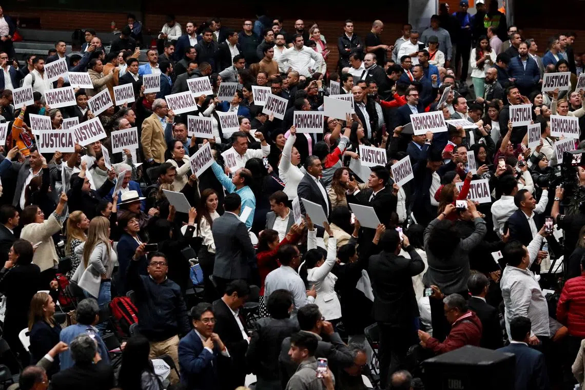 Lawmakers raise posters reading \"Democracy\" and \"Justice\" after approving the judicial reform proposed by Mexico's President Andres Manuel Lopez Obrador, at the Magdalena Mixhuca Sports Complex, in Mexico City, Mexico September 4, 2024. REUTERS/Henry Romero