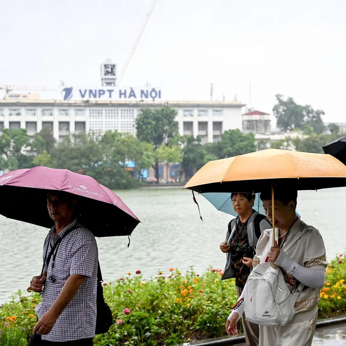 Tourists walk under umbrellas to shelter from the rain along Hoan Kiem Lake in Hanoi on October 14, 2025. (Photo by Nhac NGUYEN / AFP)