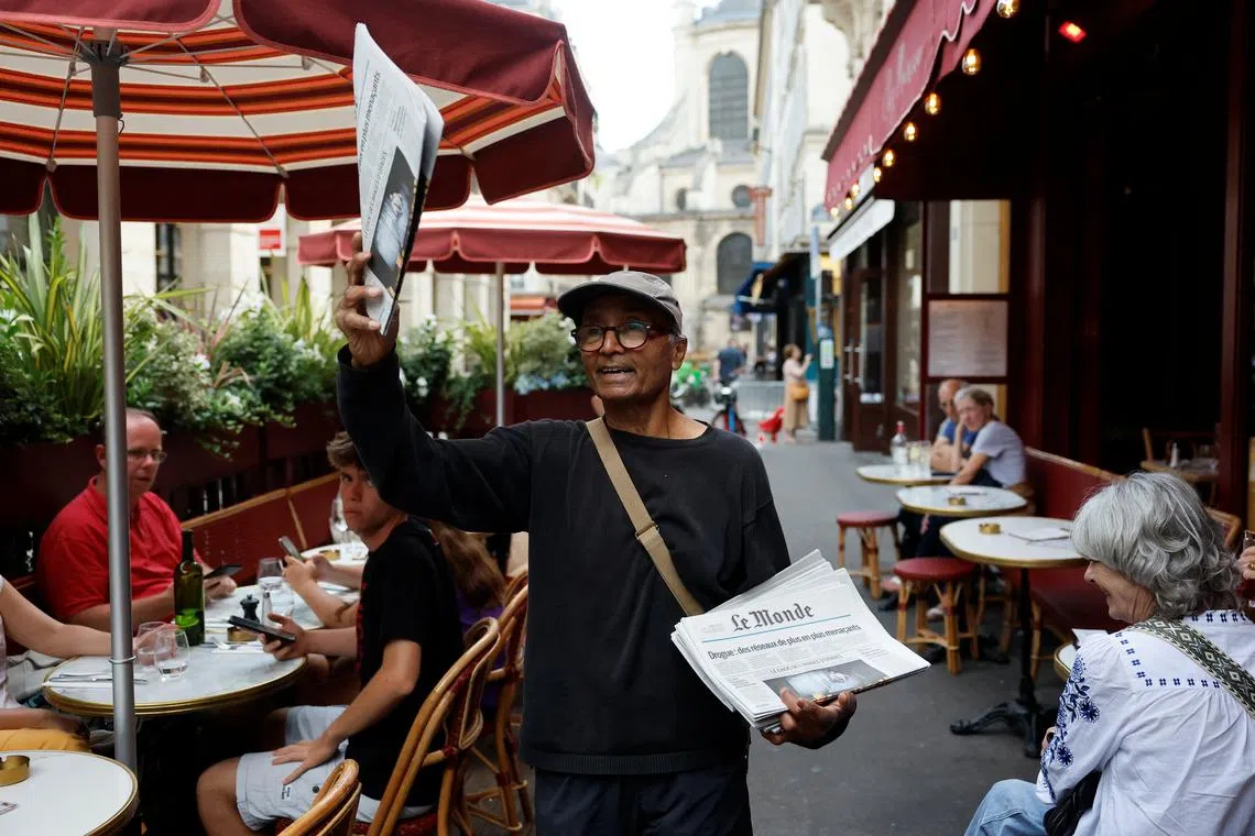 Ali Akbar, 73, known as the last newspaper hawker in the French capital sells 'Le Monde' newspaper to people on a terrace in the Latin Quarter, in Paris, France, August 4, 2025. REUTERS/Stephanie Lecocq