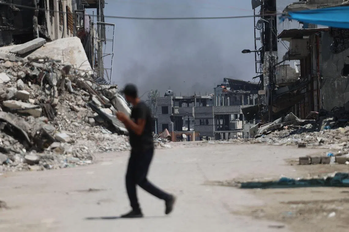 TOPSHOT - A Palestinian man crosses a street with smoke billowing in the background from an area targeted by Israeli bombardment in the Gaza City district of Shujaiya on June 28, 2024, amid the ongoing conflict between Israel and the militant Hamas group. Israel's military said on June 28 it was conducting raids backed by air strikes in northern Gaza, killing "dozens" of militants in an area where it had declared the command structure of Hamas dismantled months ago. The operation in Shujaiya, on the edge of Gaza City, caused numerous casualties, witnesses and medics said the previous day when it began. (Photo by Omar AL-QATTAA / AFP)