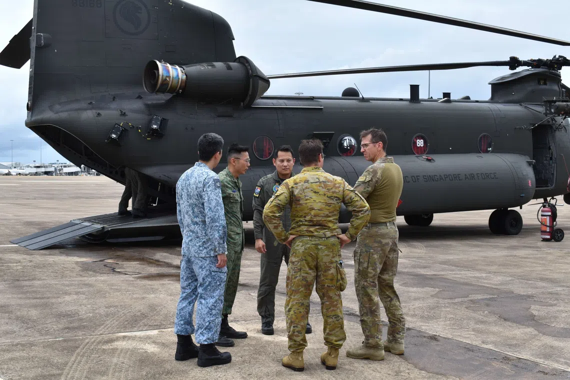 Personnel from the RSAF and the ADF discussing flood relief operations as the helicopter is being prepared.