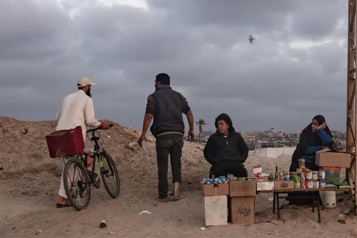 People walk past a displaced Palestinian family's food stall, on the beach in a refugee camp in Rafah, in the southern Gaza Strip.