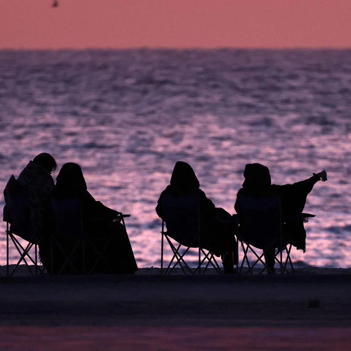 Women sit along the beach at sunrise, in Kuwait City on April 15, 2023. (Photo by YASSER AL-ZAYYAT / AFP)