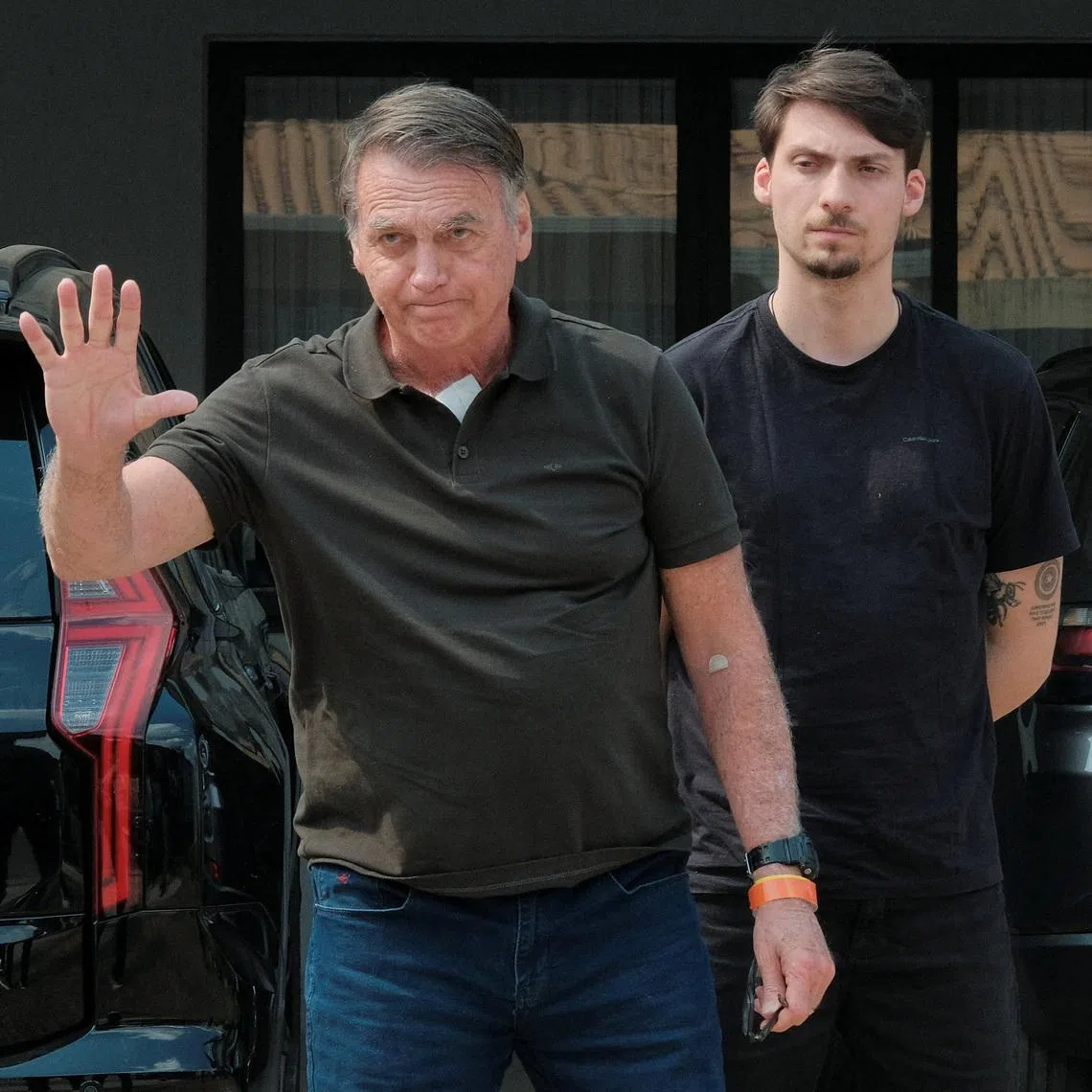 Former Brazilian President Jair Bolsonaro gestures accompanied by his son Jair Renan Bolsonaro after he arrived to his house from the hospital where he went to undergo a skin surgery procedure, authorized by Supreme Court Justice Alexandre de Moraes, after being convicted by a Supreme Court majority of plotting a coup to remain in power after losing the 2022 election, in Brasilia, Brazil, September 14, 2025. REUTERS/Diego Herculano/File Photo