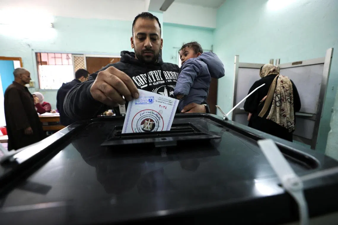 A man, holding a child, votes at a polling station during the first day of the presidential election in Cairo, Egypt on Dec 10.
