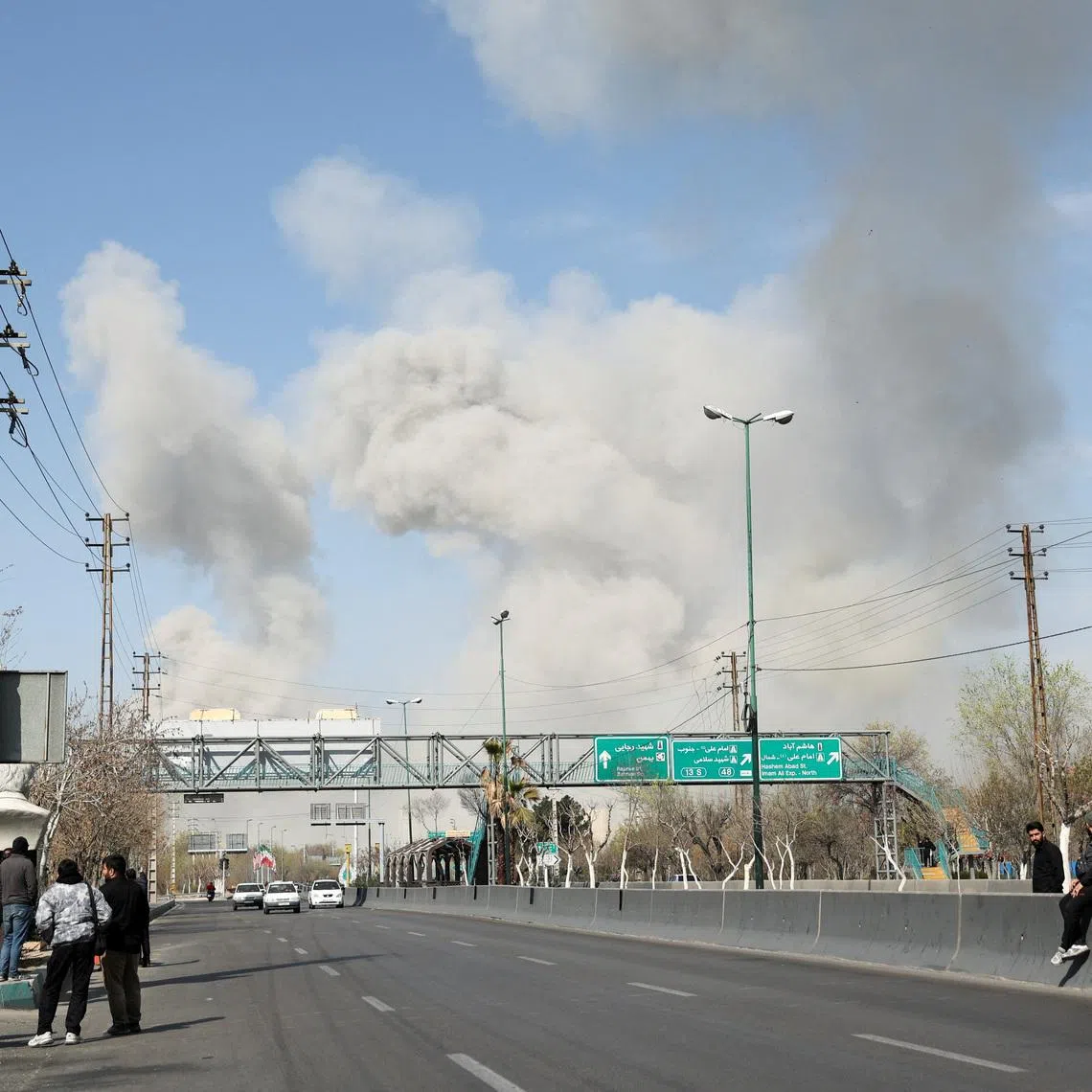 People gather on the sides of a road as smoke rises in the background following an explosion, amid the U.S.-Israeli conflict with Iran, in Tehran, Iran, March 5, 2026. Majid Asgaripour/WANA (West Asia News Agency) via REUTERS