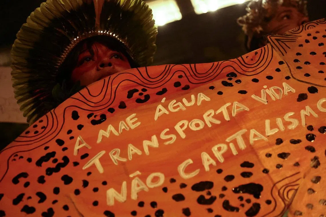 A protester shows a sign that reads \"Mother water transports life, not capitalism\" during a demonstration at Cargill's offices in support of Indigenous groups who have been blocking truck traffic for several days at the entrance of Cargill's Santarem terminal in northern Brazil, protesting against plans to dredge the Tapajos river and move more grains like soy and corn destined for export markets, in Sao Paulo, Brazil, February 20, 2026. REUTERS/Jean Carniel