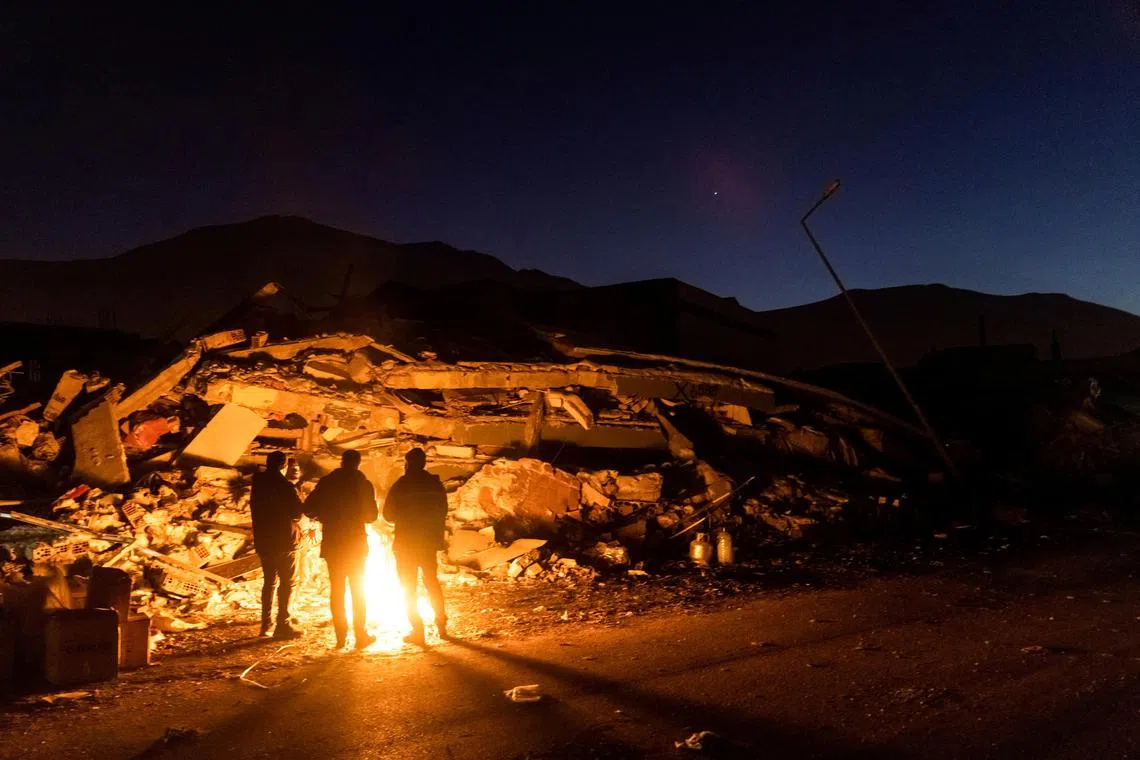 People stand by a fire next to remains of a destroyed building in Elbistan, Turkey, on Feb 14, 2023.