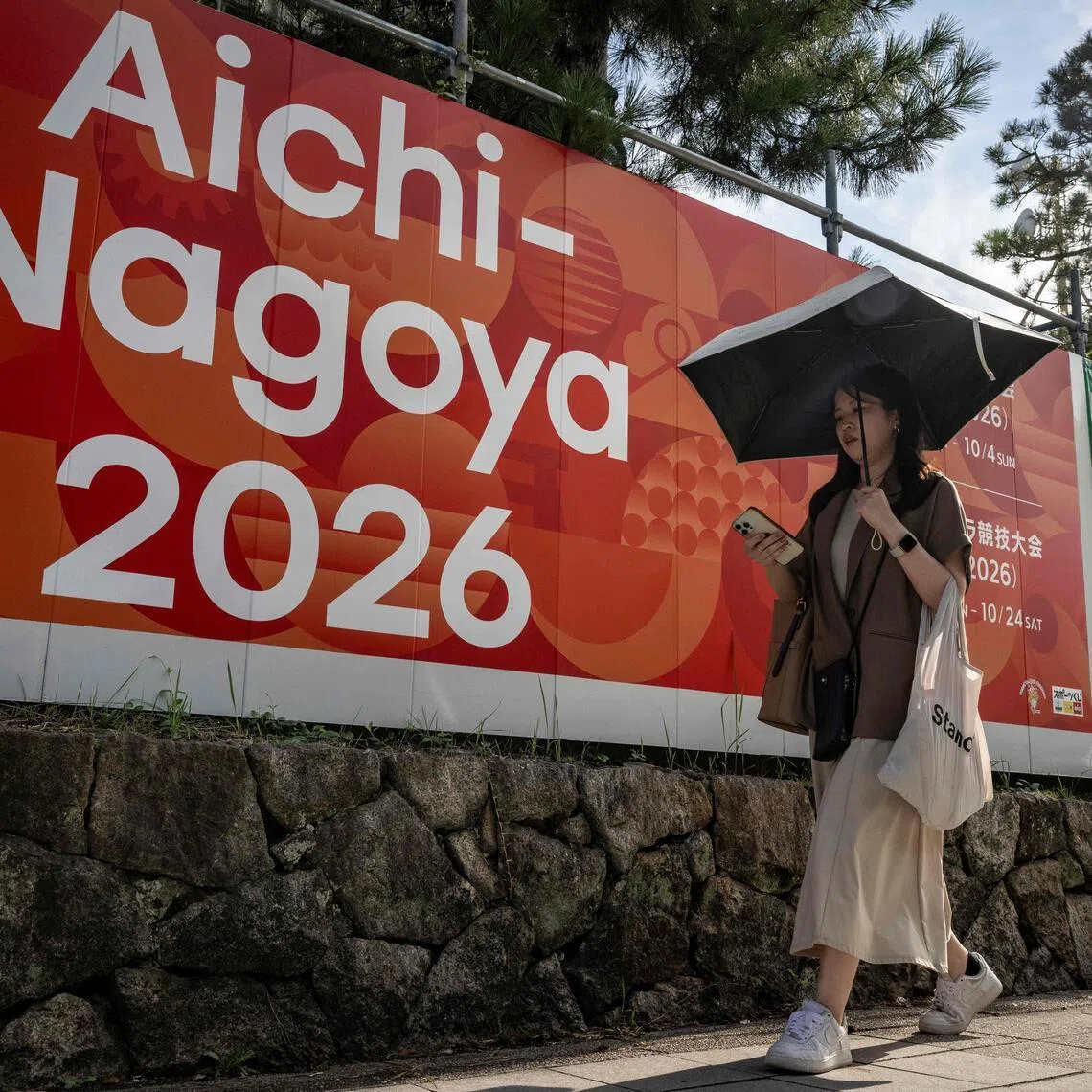 This picture taken on September 8, 2025, shows a woman walking past an advertisement for the 2026 Aichi-Nagoya Asian Games in Nagoya, Aichi prefecture. The Games will take place from Sept 19 to Oct 4, 2026.