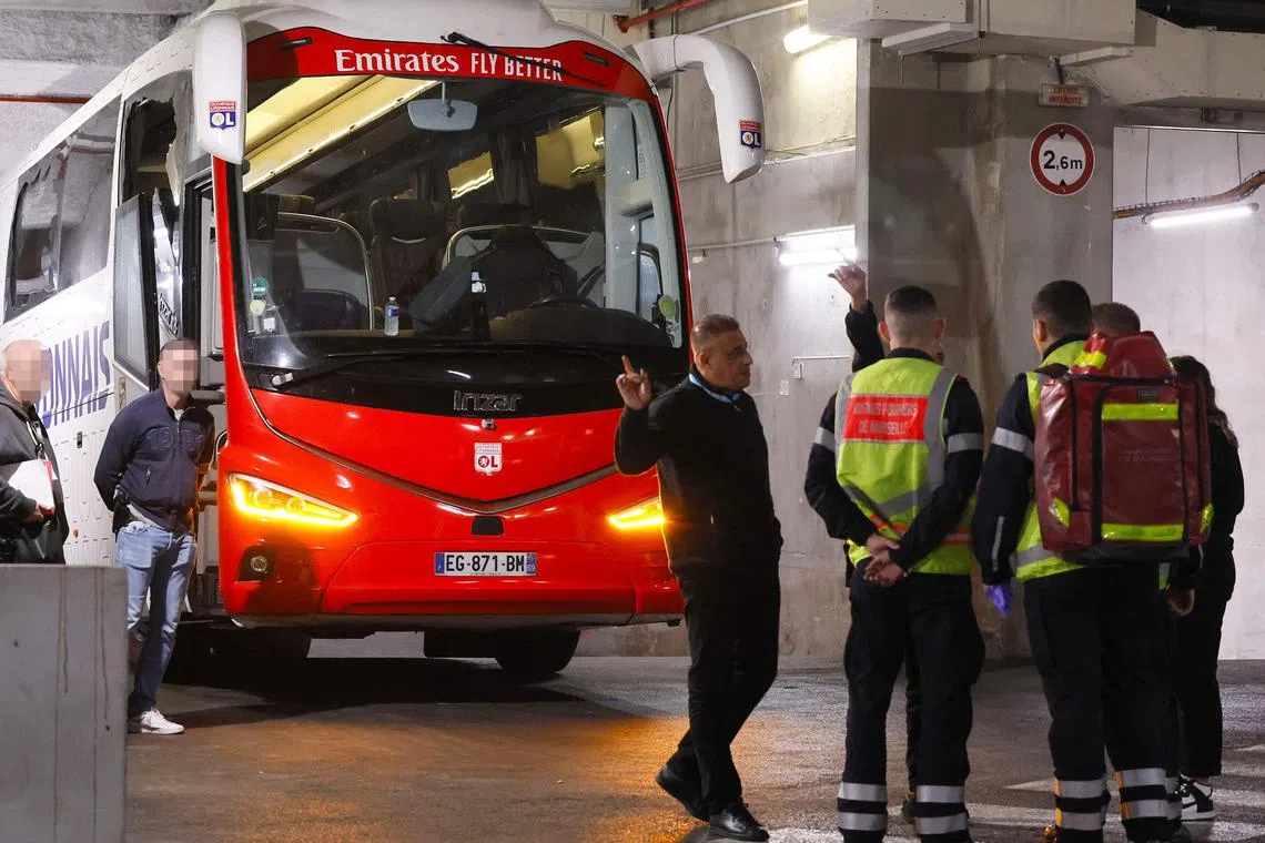 Firefighters standing next to Lyon's team bus, showing one window completely broken and another damaged, after the bus was stoned as it entered the Stade Velodrome ahead of the match between Marseille and Lyon at Stade Velodrome in Marseille.