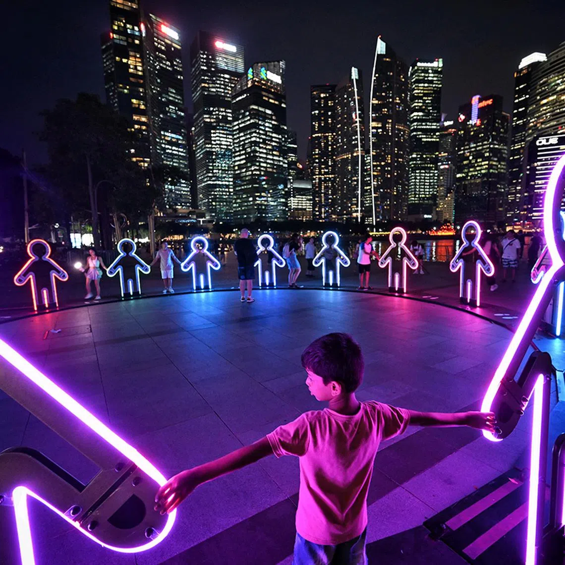 (SUGGESTED MAIN PIC #2) Embrace by Beamhacker (Australia), presented by Defence Collective Singapore at Event Square, features life-sized silhouettes inspired by children's paper chains. When visitors hold the hands of the figures, ripples of light and sound are triggered, culminating in a full symphony when the circle is completed. The installation evokes the joy of childhood play while symbolising unity between Singapore’s military and civilians. The silhouettes, adorned with camouflage patterns representing the four SAF services, stand as a tribute to collective strength. A commissioned score by Peter McAvan accompanies the experience.