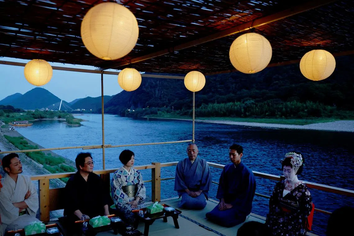 Houkan (male counterpart to Geisha) Tatsuji, 29, and Maiko (apprentice female Geisha), Kikuyu, 20, sitting with visitors to watch cormorant fishing or ukai, at a riverside observation deck in the Nagara River, during a trial organized by the nonprofit organization ORGAN in Gifu, Japan, Sept 13, 2023. 