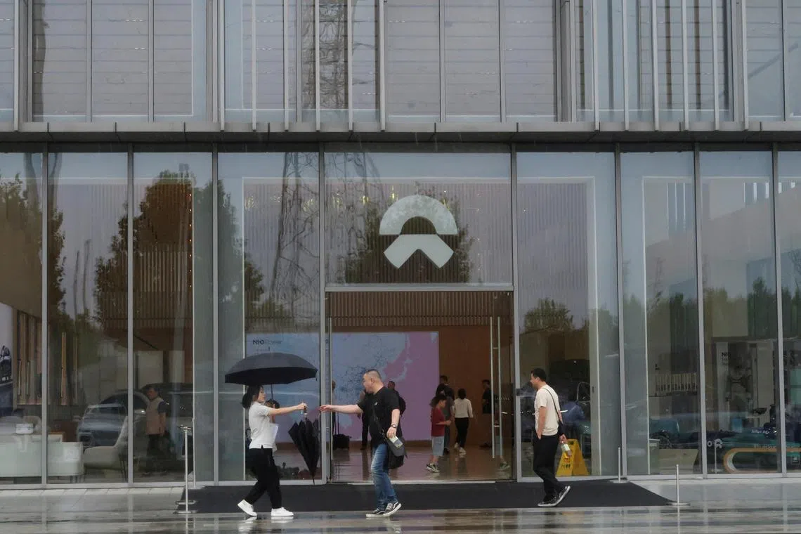 A staff member hands an umbrella to a man outside a store of Chinese electric vehicle (EV) maker Nio at the company's manufacturing base in Hefei, Anhui province, China June 28, 2024. REUTERS/Ellen Zhang