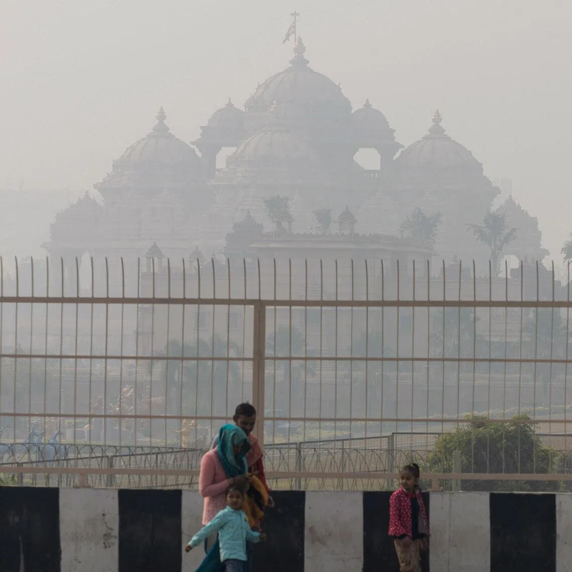 A family walks past the Akshardham temple, shrouded in heavy smog and air pollution, in New Delhi, India, on Dec 19.