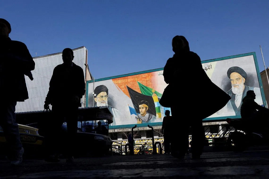 People walk near a mural featuring images of Iran's Supreme Leader Ayatollah Ali Khamenei and the leader of Iran's 1979 Islamic Revolution Ayatollah Ruhollah Khomeini on a street in Tehran, on Feb 17.