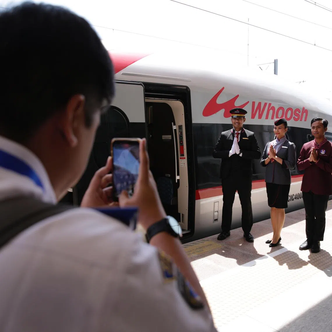epa10894934 A man takes a picture of rail workers standing next to the Jakarta-Bandung High-Speed Train during an inauguration ceremony, lead by Indonesian President Joko Widodo (not pictured), at Halim Station in Jakarta, Indonesia, 02 October 2023. Joko Widodo inaugurated the Jakarta-Bandung High-Speed Train at Halim Station. The Jakarta-Bandung high-speed train, named Whoosh, is the first in Indonesia and also the first in Southeast Asia. This fast train has a maximum speed of 350 kilometers per hour.  EPA-EFE/ADI WEDA