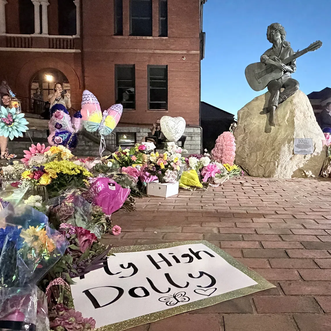 Mourners pay their respects to Dolly Parton after the announcement of her passing, at the Dolly Parton Statue in downtown Sevierville, Tennessee, U.S., August 25, 2026. Picture taken with a mobile phone. REUTERS/Kevin Fogarty