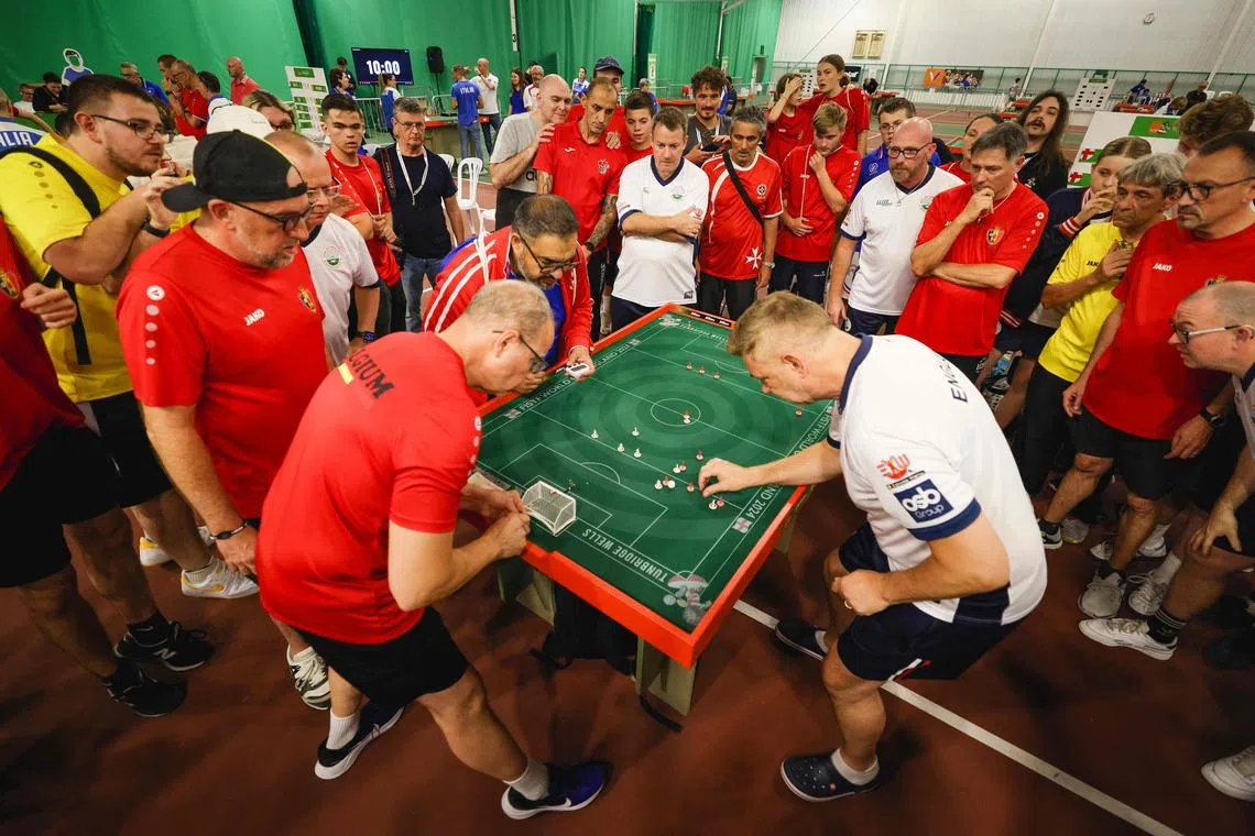 TOPSHOT - People look on as England veteran player Darren Clarke (R) takes a shot against Belgium during the Subbuteo World Cup in Tunbridge Wells in south east England, on September 22, 2024. A three-day table-football  tournament, which ended on Sunday, saw 300 of the world's elite from 26 nations jet into the southern England town of Tunbridge Wells, the "spiritual home" of table-football where the iconic game Subbuteo -- which was later copied around the world -- was invented in 1946. (Photo by Adrian DENNIS / AFP)