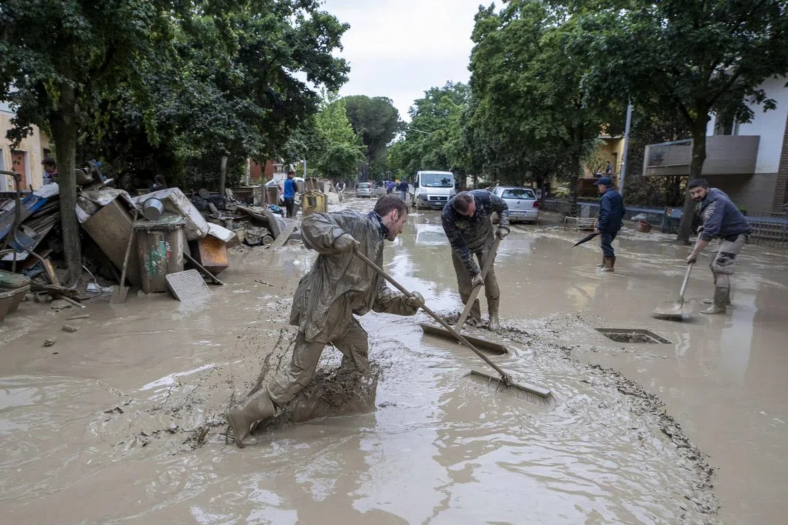 People work to clean a water-logged street following the flood that is affecting Emilia-Romagna region, in Faenza, Italy, on May 19 2023. 
