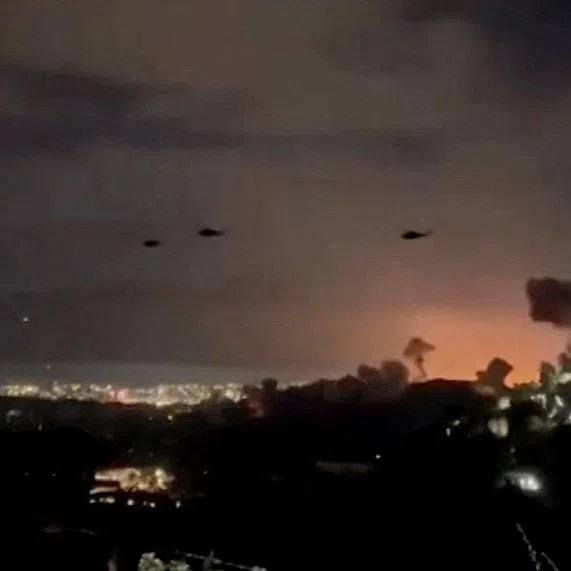 Helicopters fly past plumes of smoke rising from explosions, in Caracas, Venezuela, on Jan 3.