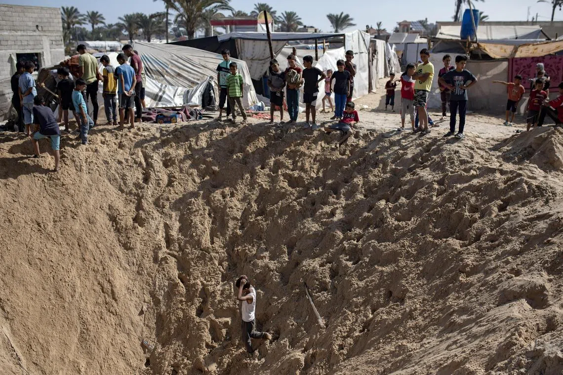 Palestinians inspect a shell crater after an Israeli military strike near their tents at a camp for displaced people in Khan Yunis, southern Gaza Strip, on June 21, 2024.