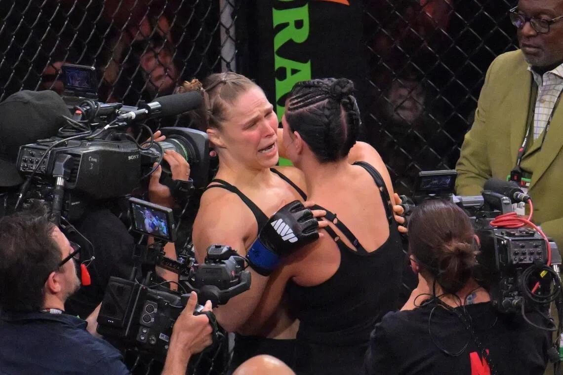 Ronda Rousey (blue gloves) embracing Gina Carano (red gloves) after a women's featherweight bout at Intuit Dome on May 16.