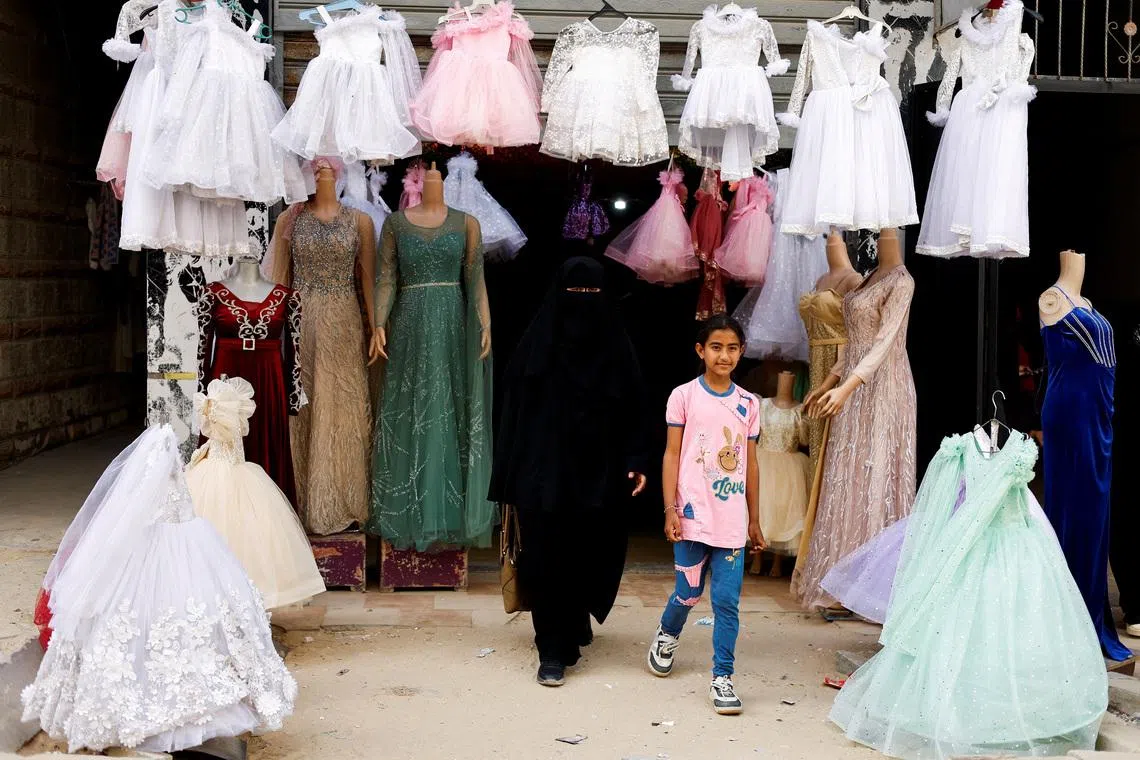 A Palestinian woman and a girl walk out of a wedding dress shop, as brides in Gaza turn to reused gowns amid soaring prices and shortages caused by the war, in Khan Younis in the southern Gaza Strip, May 9, 2026. REUTERS/Mahmoud Issa