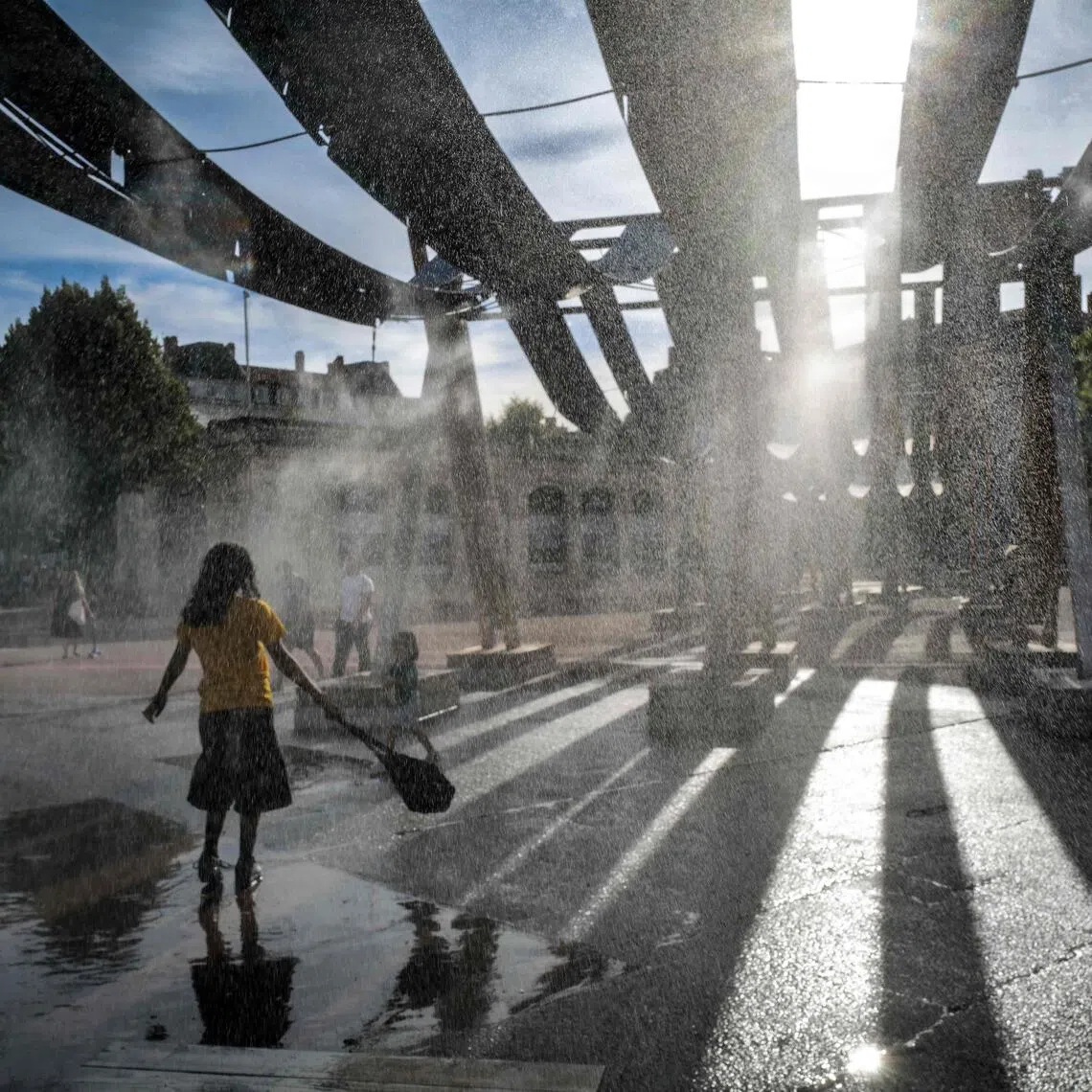 Pedestrians walk through water sprays on Place Bellecour during a heatwave in Lyon, central France.
