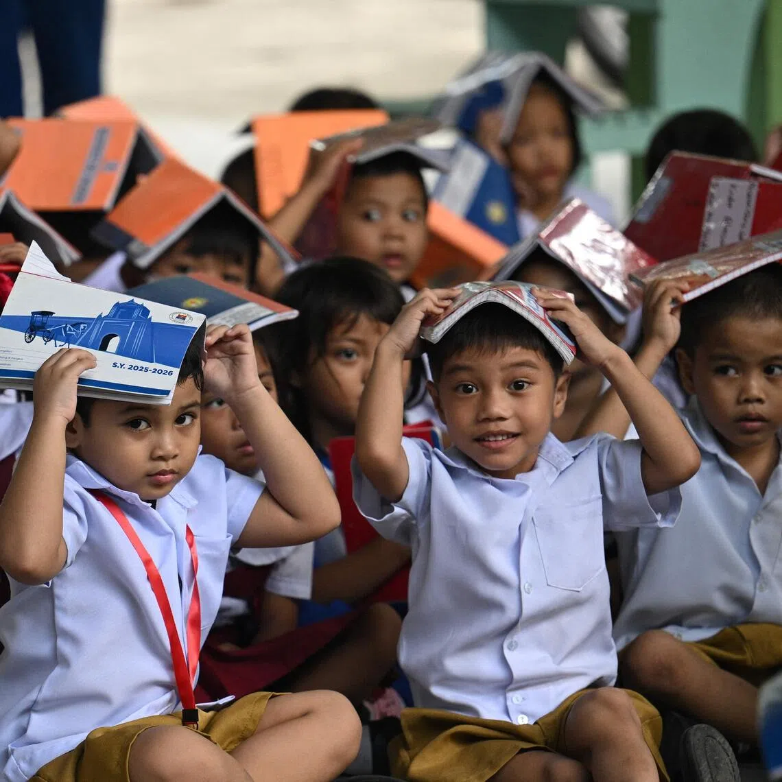 Young students place books and notebooks on their heads as they gather at a designated evacuation center outside a school building during an earthquake drill as part of the government's annual simulation at a an elementary school in Manila on September 11, 2025. (Photo by Ted ALJIBE / AFP)
