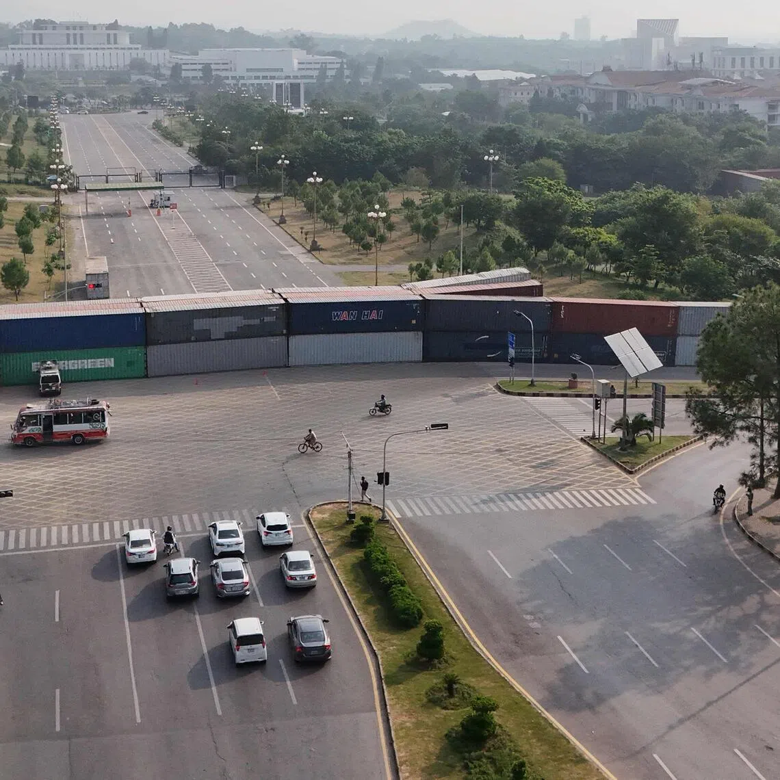 Commuters driving past shipping containers placed by authorities to block access towards the President’s House and the Red Zone area in Islamabad on Sept 24.