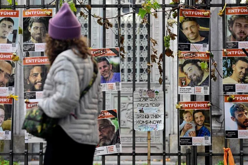 A woman passes a placard saying 'bring them home now' placed among portraits of hostages and victims of militant group Hamas on a fence in Berlin on Oct 6.
