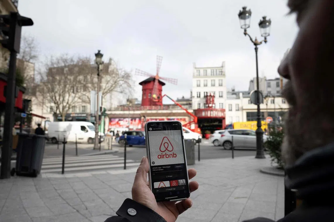 A woman holds up her mobile phone with the short- and long-term homestays app Airbnb on the screen as she stands close to the Moulin Rouge cabaret in central Paris on February 2, 2024, as the city prepares for the upcoming Paris 2024 Olympic Games which are set to take place from July 26 to August 11. (Photo by Miguel MEDINA / AFP)