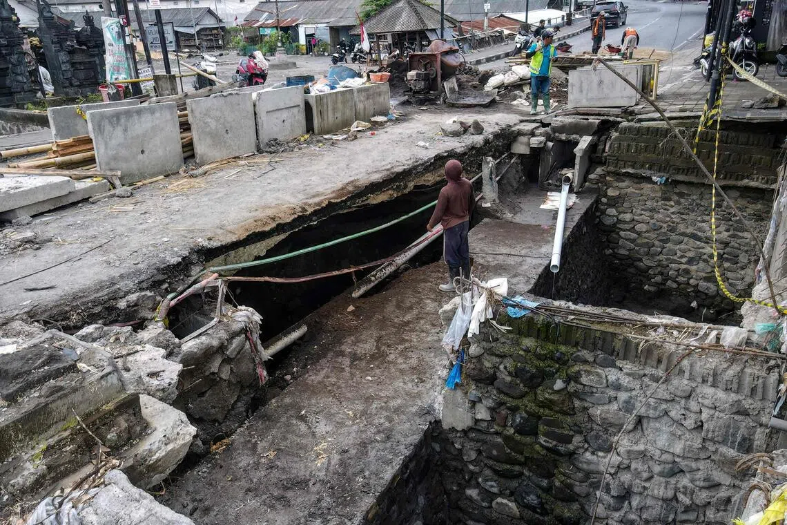 This picture taken on October 1, 2025 shows workers repairing an area where a large sinkhole formed during recent flooding in Badung, on Indonesia's resort island of Bali. Devastating flash floods that killed at least 18 people and left four missing was the island's worst in a decade, according to Indonesia's Meteorology, Climatology and Geophysics Agency (BMKG). It was caused partly by record rain, but was also a reckoning for years of rampant overdevelopment and a waste management system under enormous strain. (Photo by BAY ISMOYO / AFP) / To go with AFP STORY Indonesia-Bali-flood-climate-waste, Focus by Marchio GORBIANO