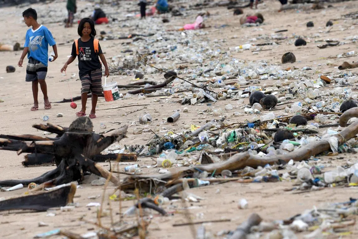 Children walk past plastic and other debris washed ashore at Kedonganan Beach, Badung regency, on Indonesia's resort island of Bali on April 12, 2023. (Photo by SONNY TUMBELAKA / AFP)