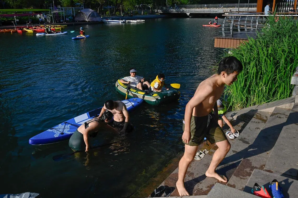 People swim and paddle in the Liangma River as they cool off amidst soaring temperatures, in Beijing on June 9, 2024.