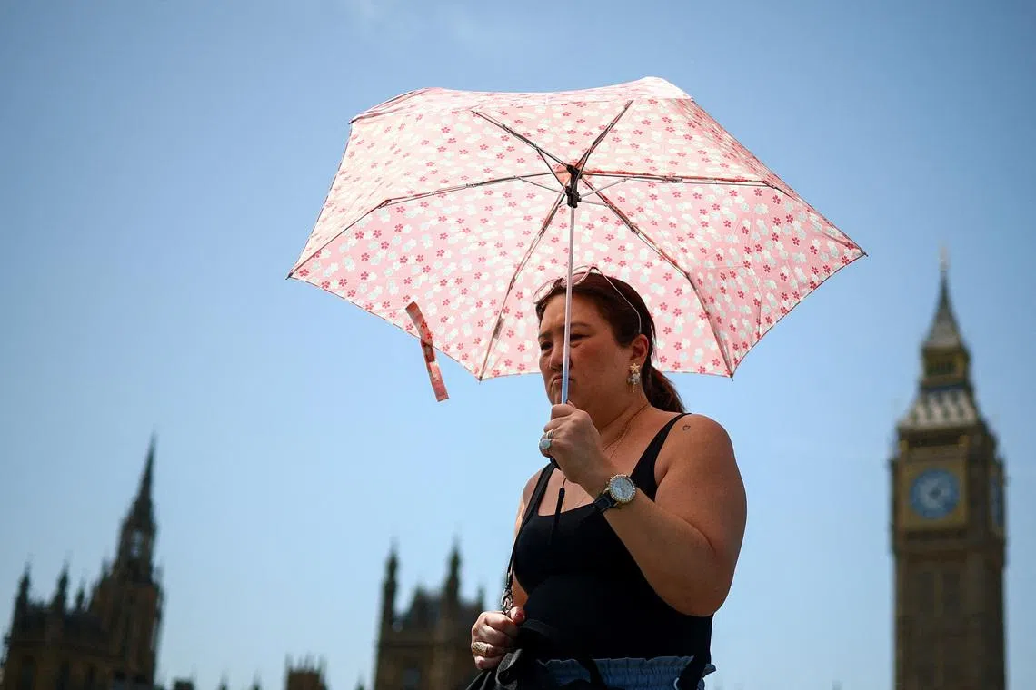 A woman uses an umbrella to shield herself from the sun as she walks near the Houses of Parliament, amid hot weather in London, Britain, June 23, 2026. REUTERS/Guglielmo Mangiapane/File Photo
