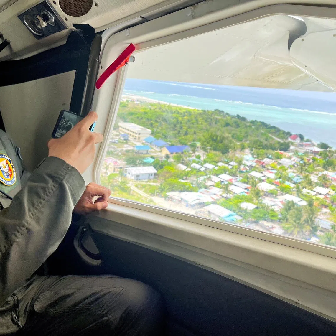 A Philippine Coast Guard member uses his phone to record the view of Philippine-occupied Thitu Island while onboard a plane in the disputed South China Sea, February 21, 2026. Picture taken with a mobile phone. REUTERS/Karen Lema