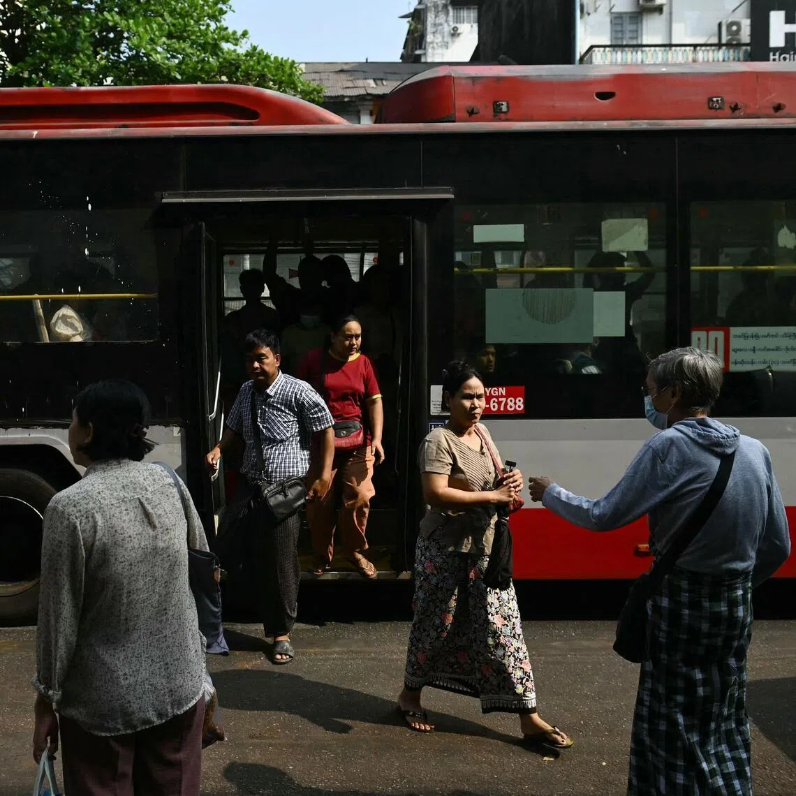 Commuters alight from a bus on the first day of the implementation of an "odd-even" vehicle numbering system in Yangon on March 7, 2026. Myanmar's junta announced half of private vehicles will be ordered off the roads each day, based on licence plate numbers, in order to conserve fuel due to the war in the Middle East. 