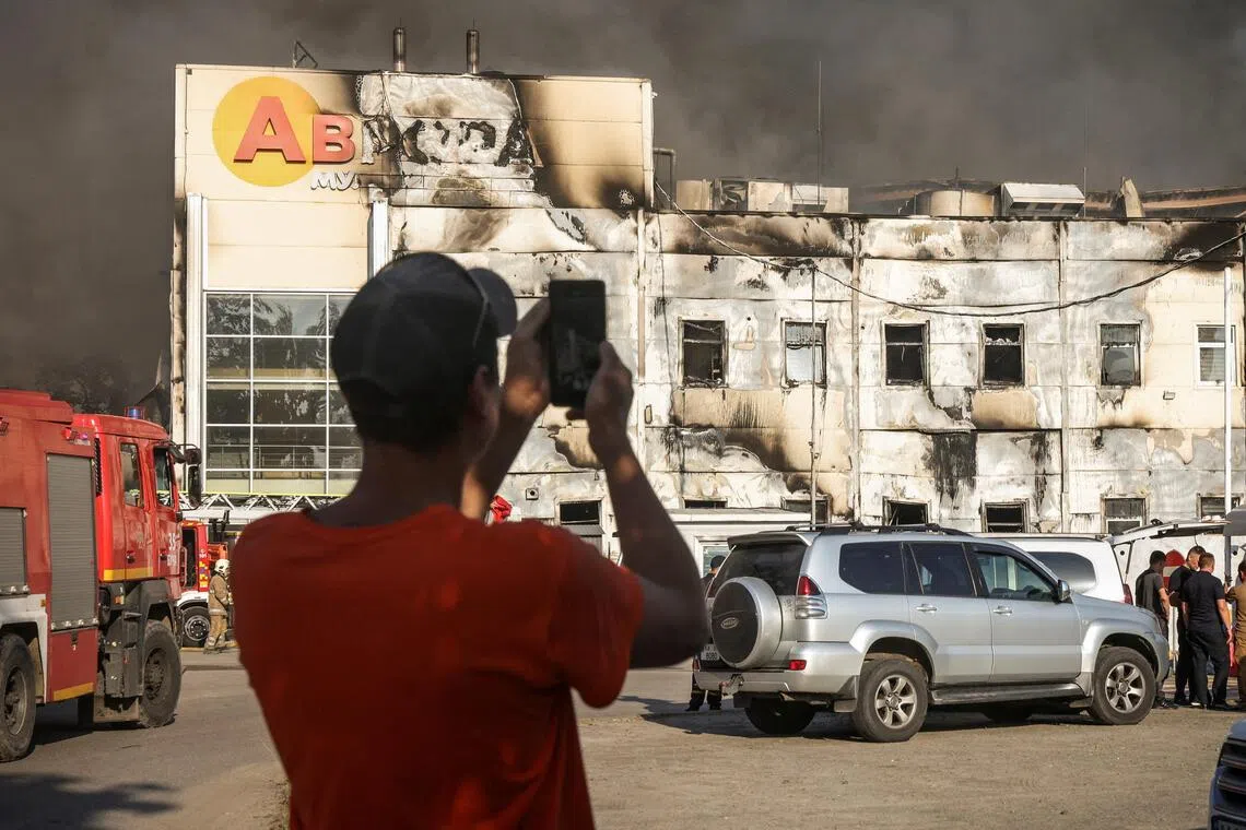A man taking a photo on Aug 31 of firefighters working at the site of a Russian drone strike on a warehouse in the Kyiv region.