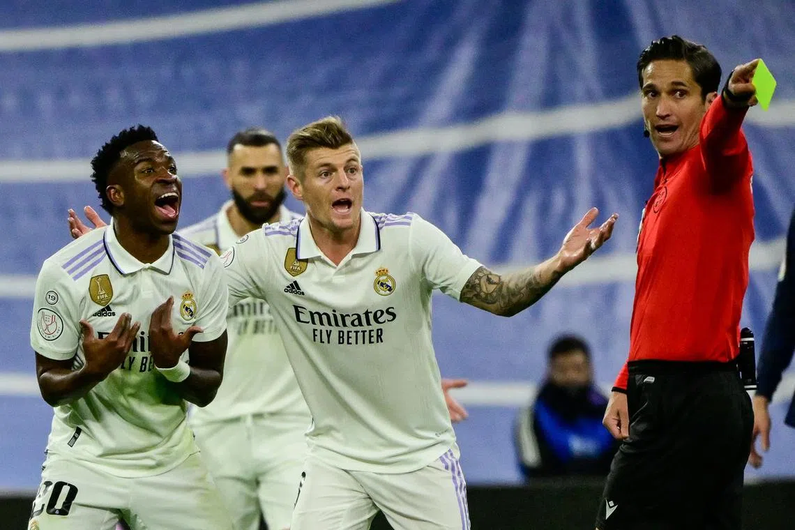 Real Madrid's Vinicius Junior (left) reacts as he receives a yellow card during a match between Real Madrid CF and FC Barcelona.