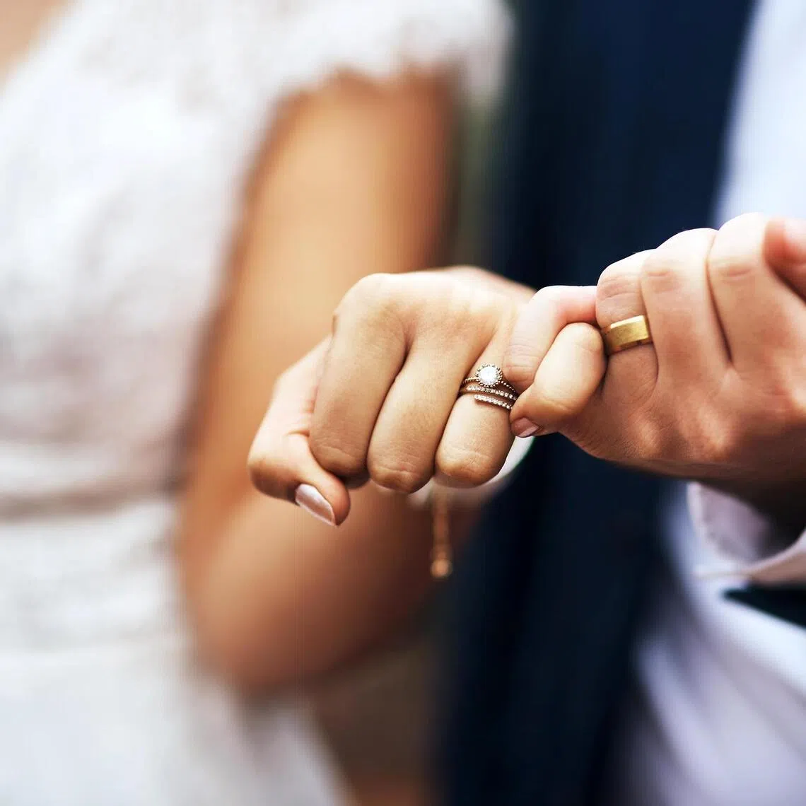 A newlywed couple doing a pinky swear gesture on their wedding day.